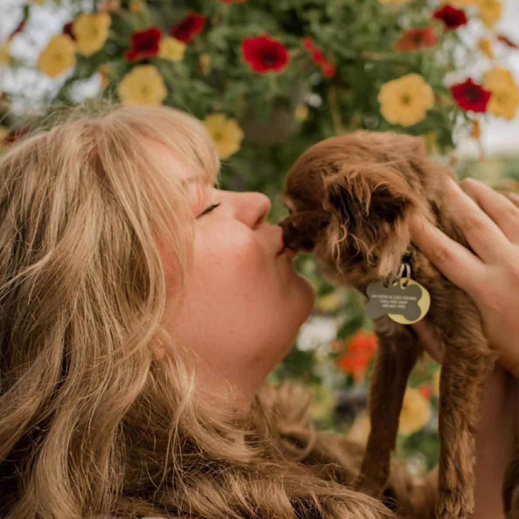 Woman kissing small brown dog outdoors.