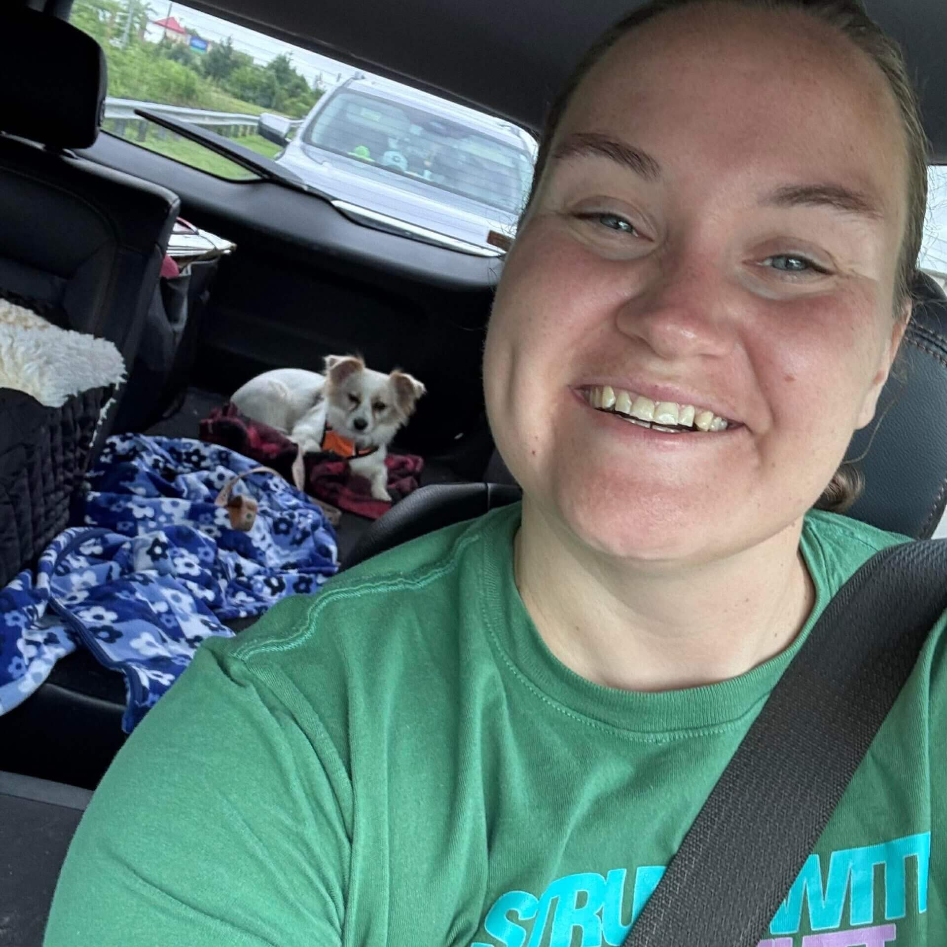 Smiling woman driving with dogs in backseat.