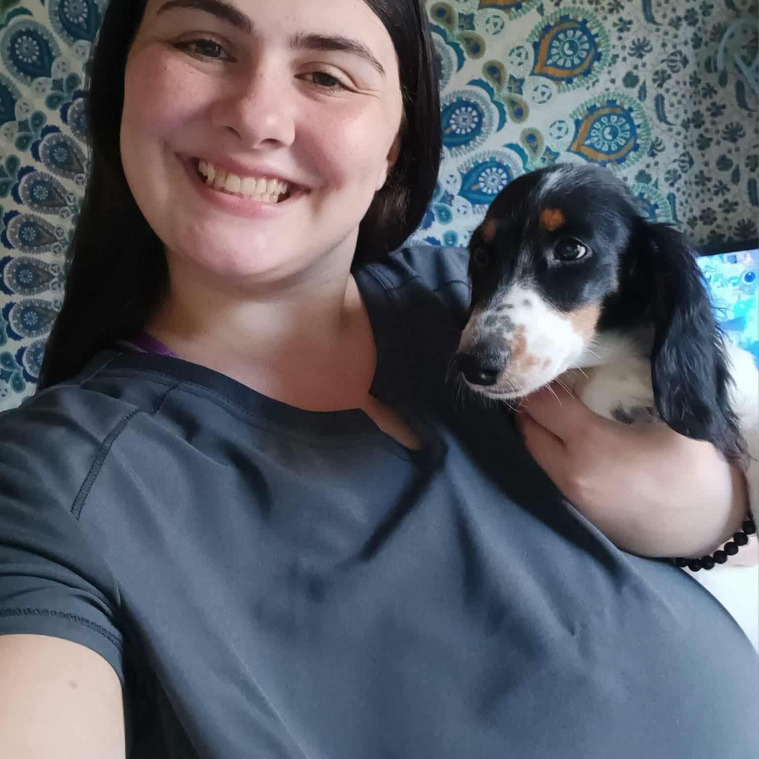 Smiling person holding a small puppy indoors.