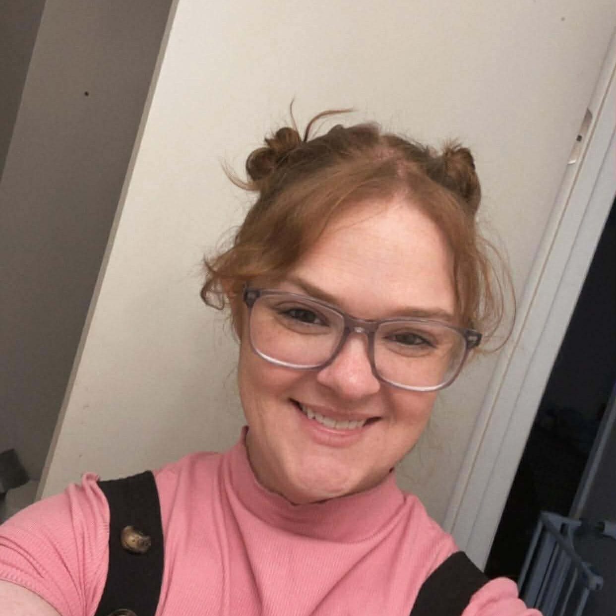 Woman smiling in glasses and pink shirt.