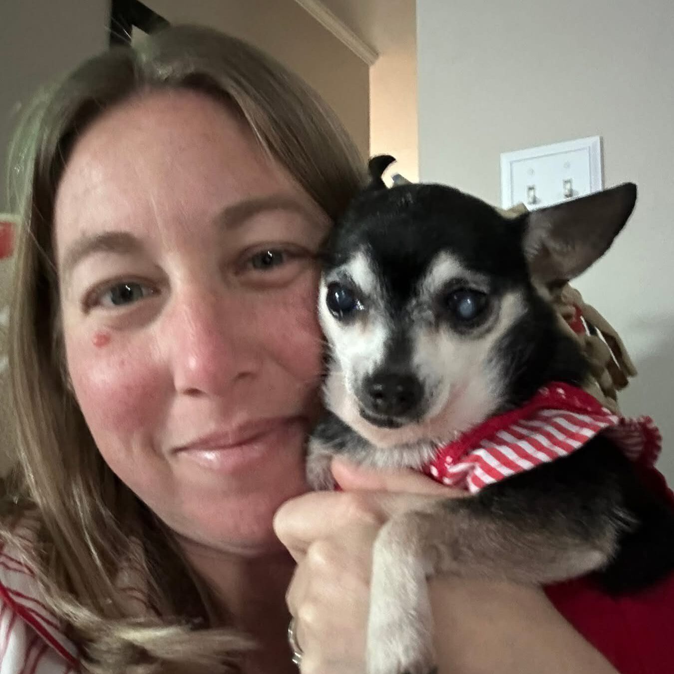 Woman holding small dog in red outfit.