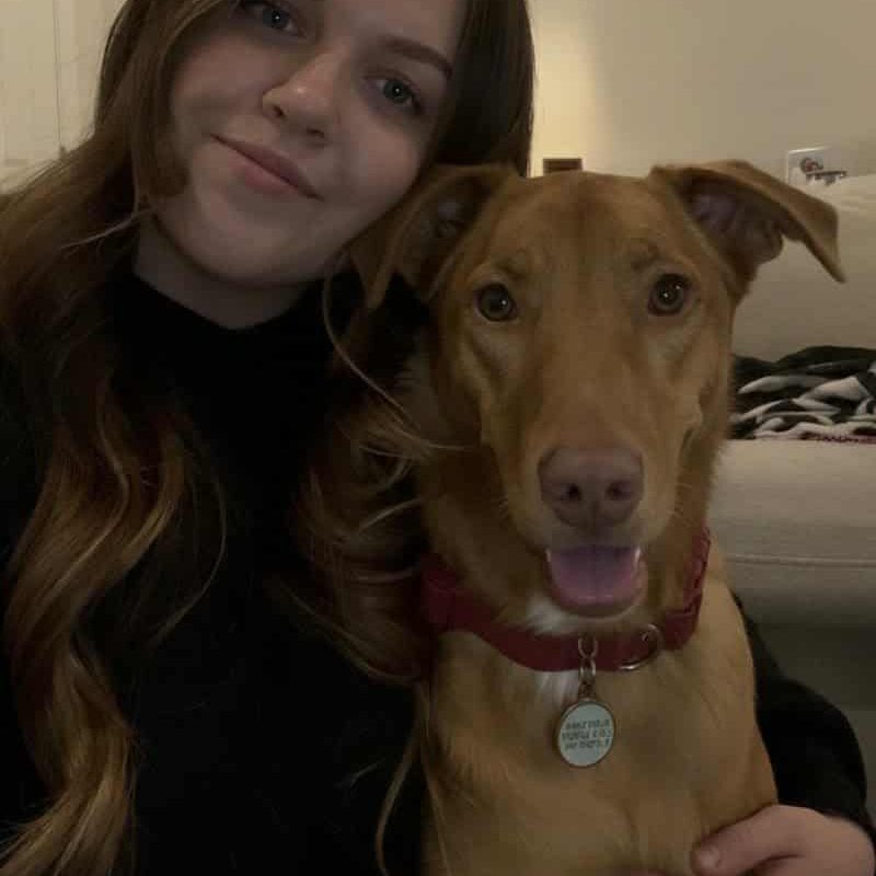Woman smiling with brown dog indoors.